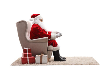 Wall Mural - Santa claus sitting in an armchair and holding a joystick