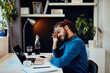 © chika_milan - Tired hipster sitting in his home office and rubbing eyes.