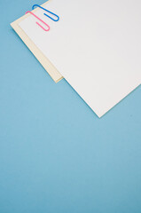 Poster - Closeup shot of a blank paper with colorful paper clips on a blue background