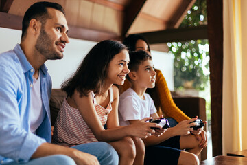 Wall Mural - Latin family enjoying the day together at home playing video games on the couch