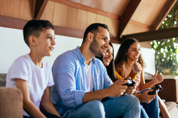 Wall Mural - Latin family enjoying the day together at home playing video games on the couch