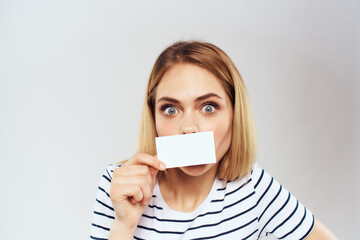 Sticker - cheerful woman in a striped t-shirt holds a business card copy Space light background