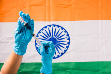 Hands of doctor wear gloves holding coronavirus (COVID-19) vial vaccine and syringe on flag India background, India Vaccination