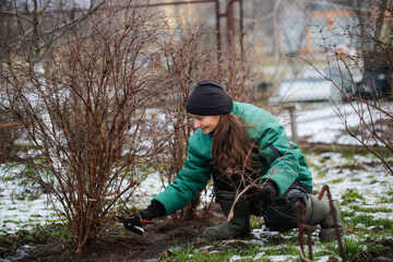 Caucasian cute woman gardener with garden tool close up, gardener pruning branches with pruning shears, winter plant pruning, winter gardening work in winter work clothes