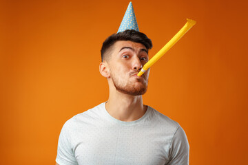 Happy man with party cone blowing into party horn