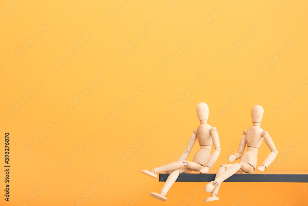 Wooden mannequins on shelf against color background