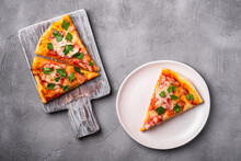 Hot Pizza Slices With Mozzarella Cheese, Ham, Tomato And Parsley On Wooden Cutting Board And Plate, Stone Concrete Background, Top View