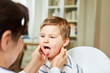 Doctor palpates tonsils on child with sore throat