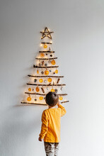 Little Child Decorating Handmade Craft Christmas Tree Made From Sticks And Natural Materials Hanging On Wall. Sustainable Christmas, Zero Waste, Plastic Free, Eco Friendly.