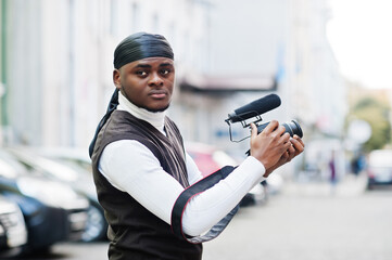 Wall Mural - Young professional african american videographer holding professional camera with pro equipment. Afro cameraman wearing black duraq making a videos.