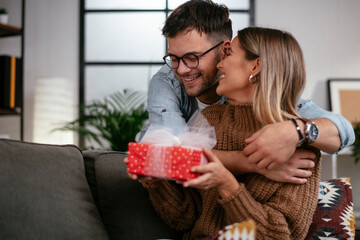 Wall Mural - Bofriend surprising his girlfriemd with a gift. Young man giving a gift box to his girlfriend.