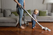 © Lisa Tichané - Happy toddler helping mother vacuum hardwood floor in living room