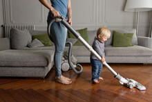 Happy Toddler Helping Mother Vacuum Hardwood Floor In Living Room