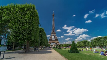 Wall Mural - Eiffel Tower on Champs de Mars in Paris timelapse hyperlapse, France. Blue cloudy sky at summer day with green lawn and people walking around