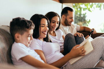 Wall Mural - Latin family enjoying the day together at home. Family reading together on the couch in the morning.