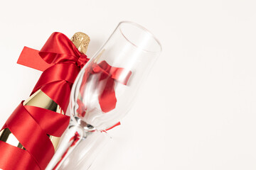 Wall Mural - empty wine glass in the foreground against the background of a bottle of champagne wrapped with a red silk ribbon on a white background