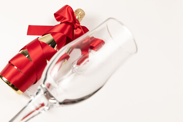 Wall Mural - empty wine glass in the foreground against the background of a bottle of champagne wrapped with a red silk ribbon on a white background