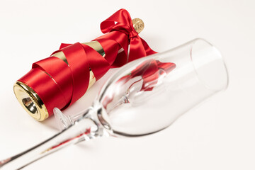 Wall Mural - empty wine glass in the foreground against the background of a bottle of champagne wrapped with a red silk ribbon on a white background