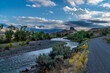 Butte and river under dramatic clouds with distance mountains and trees and shrub in the foreground, Castle Rock, South Fork Shoshone River, Cody, Wyoming