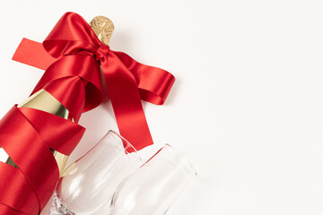 Wall Mural - gift bottle of champagne in gold foil wrapped in a red silk ribbon and two glasses on a white background