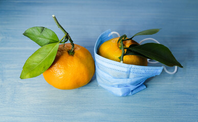 Christmas time: two mandarins on a blue background. Mandarin in a medical mask. 