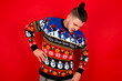 © Roquillo - Young handsome Caucasian man wearing Christmas sweater against red wall, Suffering of backache, touching back with hand, muscular pain