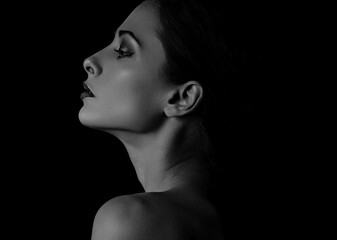 Wall Mural - Beautiful mysterious woman in darkness with healthy neck, shoulders and serious wisdom look on dramatic  black background with empty copy space. Closeup portrait. Profile view.