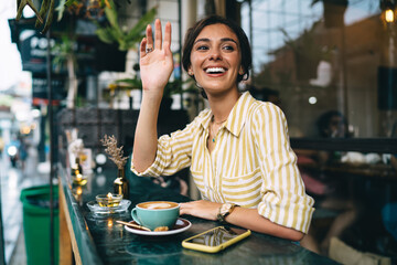 Wall Mural - Cheerful ethnic woman raising hand for greeting