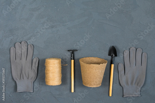 A set of garden tools with gloves and a pot for replanting flowers on a gray concrete textured background. Place for an inscription. View from above.