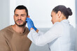 © LIGHTFIELD STUDIOS - African american doctor in latex gloves checking ear of sick patient