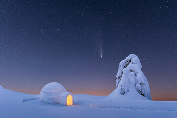 Snow igloo luminous from the inside in the winter mountains. Starry sky with comet on the background