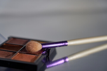 Makeup brush and shadow palette on reflective surface.