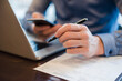 © Daniel Ingold/Westend61 - Man at desk using cell phone and holding ball pen in his hand, close-up