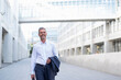 © Daniel Ingold/Westend61 - Portrait of smiling businessman walking at courtyard of modern office building