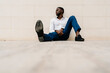 © Ezequiel Gimenez/Westend61 - Tired African entrepreneur looking away while sitting and relaxing against wall on footpath