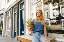 Netherlands, Maastricht, Blond Young Woman Holding Flowerpot In The City