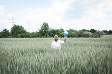 Bearded Man Holding Globe While Standing Amidst Cornfield Against Sky