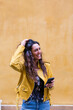 © Giorgio Magini/Westend61 - Portrait of young laughing woman wearing yellow leather jacket and holding smartphone