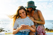 © Marco Govel/Westend61 - Smiling young female friends using smart phone against sea during sunny day
