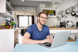 © peter scholl/Westend61 - Portrait of smiling man using laptop in kitchen at home
