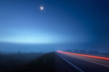 Wall Mural - Panoramic view of the empty highway through the fields in a fog at night. Moonlight. Sunrise. Europe. Transportation, logistics, travel, road trip, freedom, driving. Motion blur effect. Rural scene