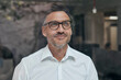 © philipp nemenz/Westend61 - Portrait of smiling man with stubble behind windowpane wearing white shirt and glasses