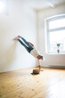 © Sebastian Moelleken I Robijn Page/Westend61 - Mature man doing a handstand on floor in empty room looking at tablet