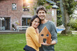 © Roger Richter/Westend61 - Portrait of smiling couple in garden of their home holding house model