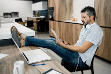 Mature Male Freelancer Holding Digital Tablet While Sitting With Feet Up On Desk At Office
