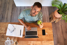 Smiling Businessman Holding Fresh Apple While Working At Home