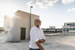 © UWE_UMSTAETTER/Westend61 - Mature man standing on roof of a high-rise building, rolling up sleeves