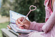 © Daniel Sierralta/Westend61 - Close-up of young woman writing in diary at park