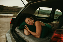 Tired Woman Sleeping In Cozy Car Trunk At Dusk