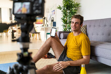 Smiling Trainer Showing Mobile Phone To Camera While Sitting At Home